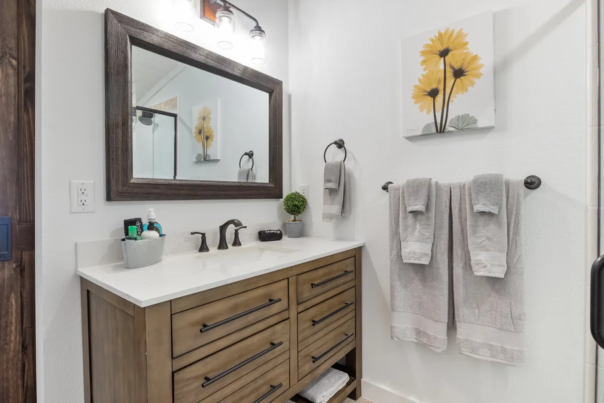 A bright bathroom vanity featuring ample storage drawers, a large mirror, sunflower-themed artwork, and towels neatly displayed. The room is filled with natural light and cheerful accents, creating a welcoming environment for daily routines.