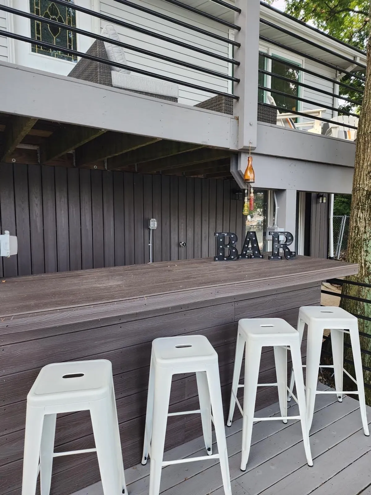 An exterior bar area featuring stools and a decorative 'BAR' sign, positioned to take advantage of sunset views. The area exudes a festive yet casual vibe, inviting guests to sit, sip cocktails, and socialize outdoors as the day transitions to night.