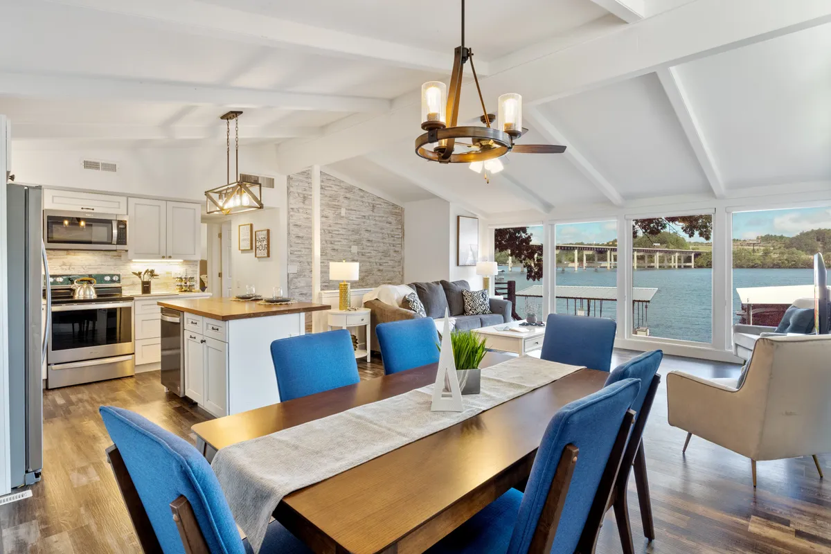 An inviting open-concept area showing a dining table and kitchen island adjacent to a sofa, with large windows framing a panoramic water view. The space feels welcoming and sociable, ideal for family meals or festive occasions.