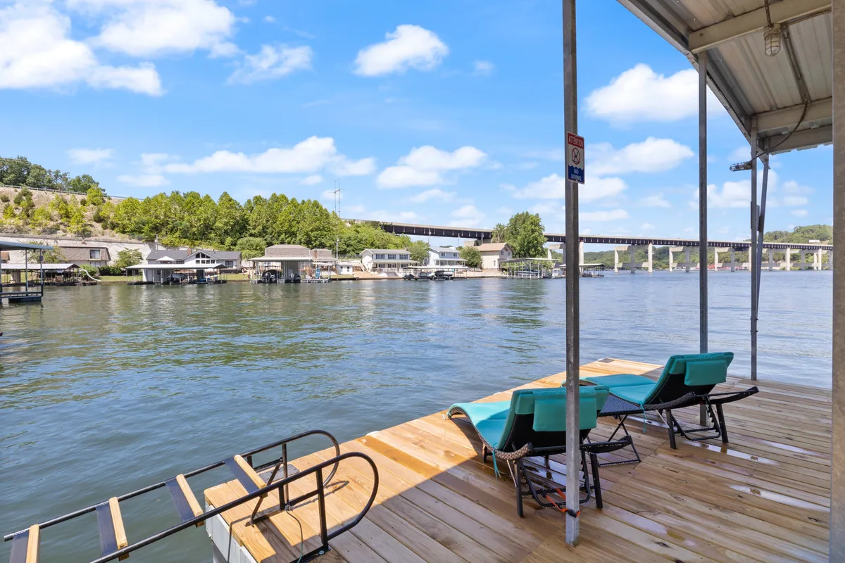 A serene lakeside dock with lounge chairs, inviting guests to sunbathe, fish, or simply enjoy panoramic water views. The bridge in the background adds visual interest and a sense of place, while the calm water enhances the peaceful mood.