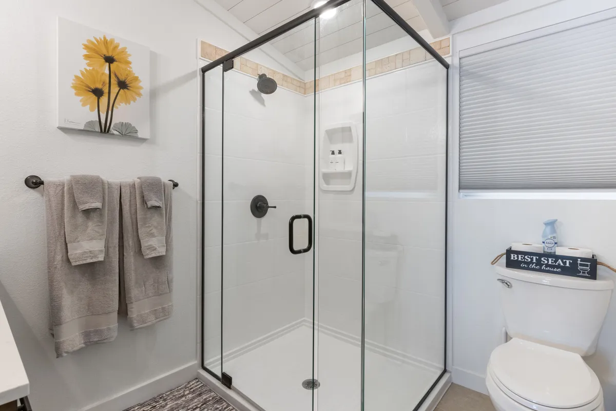 A modern, inviting bathroom with a glass shower enclosure, bright yellow floral artwork, and neatly hung towels. Clean lines and fresh details create a spa-like mood, emphasizing comfort and practical amenities.