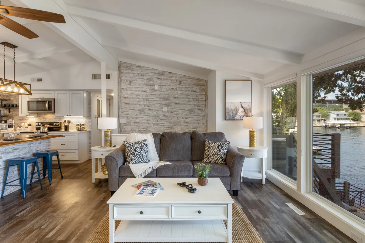 A cozy living space with a comfortable sofa, coffee table, and large windows. The kitchen area is visible in the background, showcasing the open layout and seamless connection between cooking, dining, and living spaces.