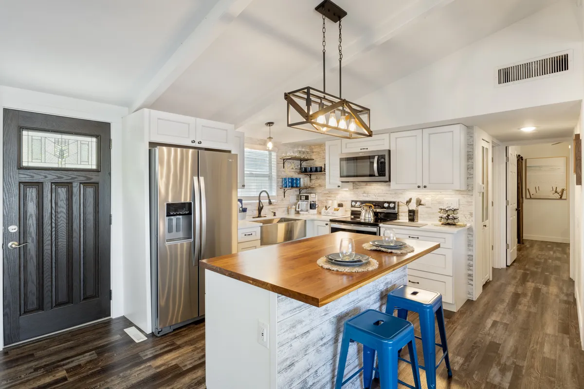 This image features a welcoming kitchen with a central island, sleek stainless steel appliances, a wooden countertop, and a stylish light fixture overhead. The arrangement invites both cooking and entertaining, capturing the essence of a chef-inspired, fully equipped kitchen.