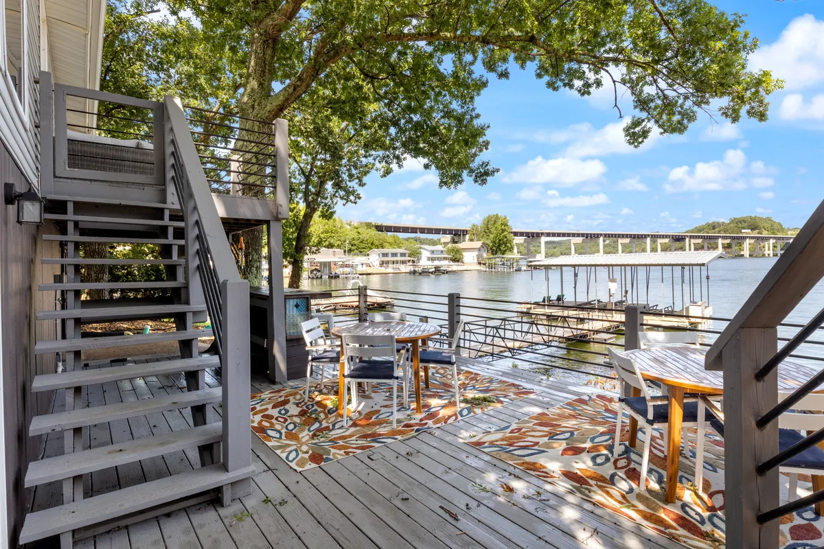 A tranquil outdoor dining area with a water view, decorative area rug, and a staircase leading down to the water. The spacious deck is ideal for group meals, sunset dinners, and socializing after attending local events.